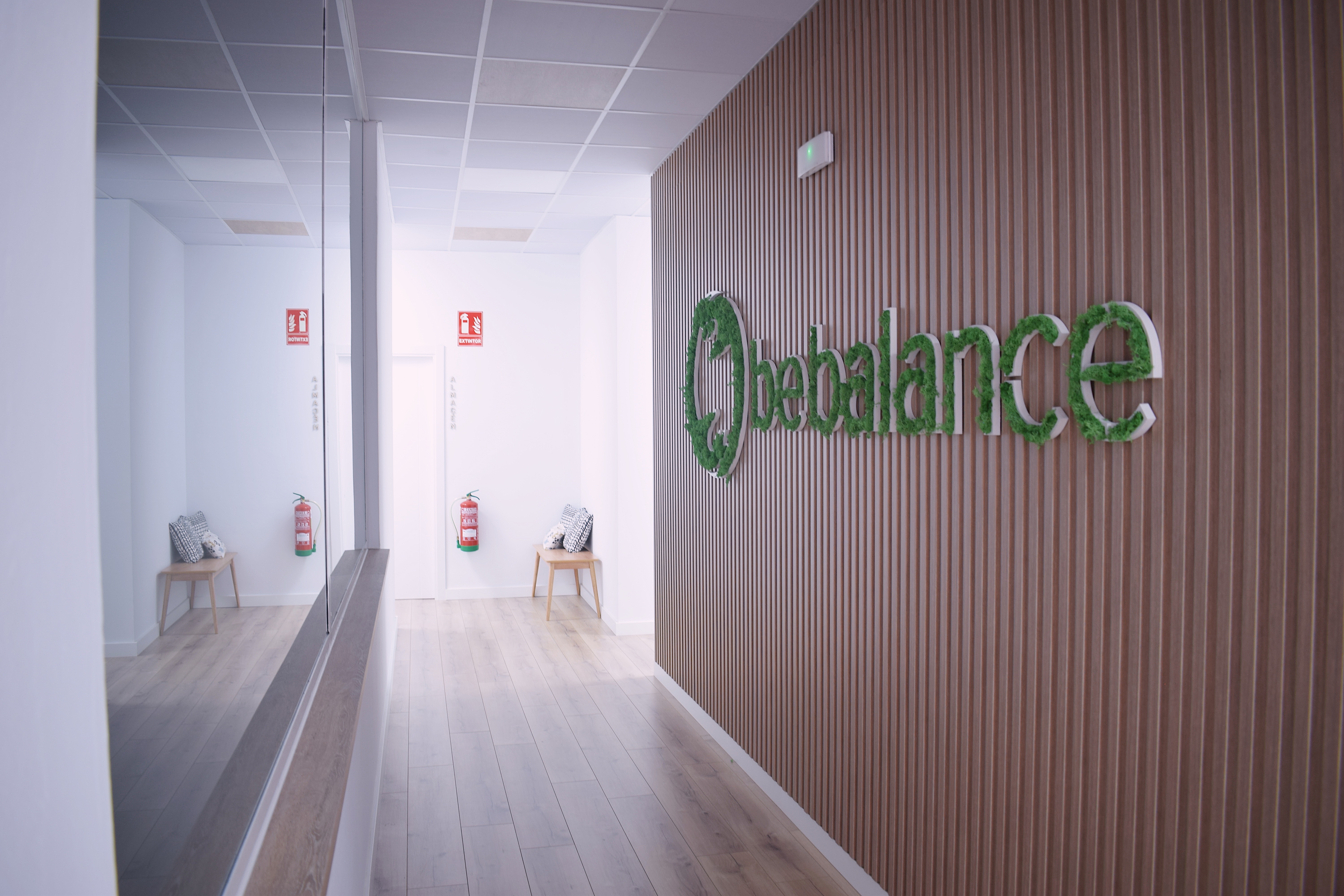 Pasillo de la clínica con el rótulo de Be Balance sobre una pared de listones de madera y un espejo