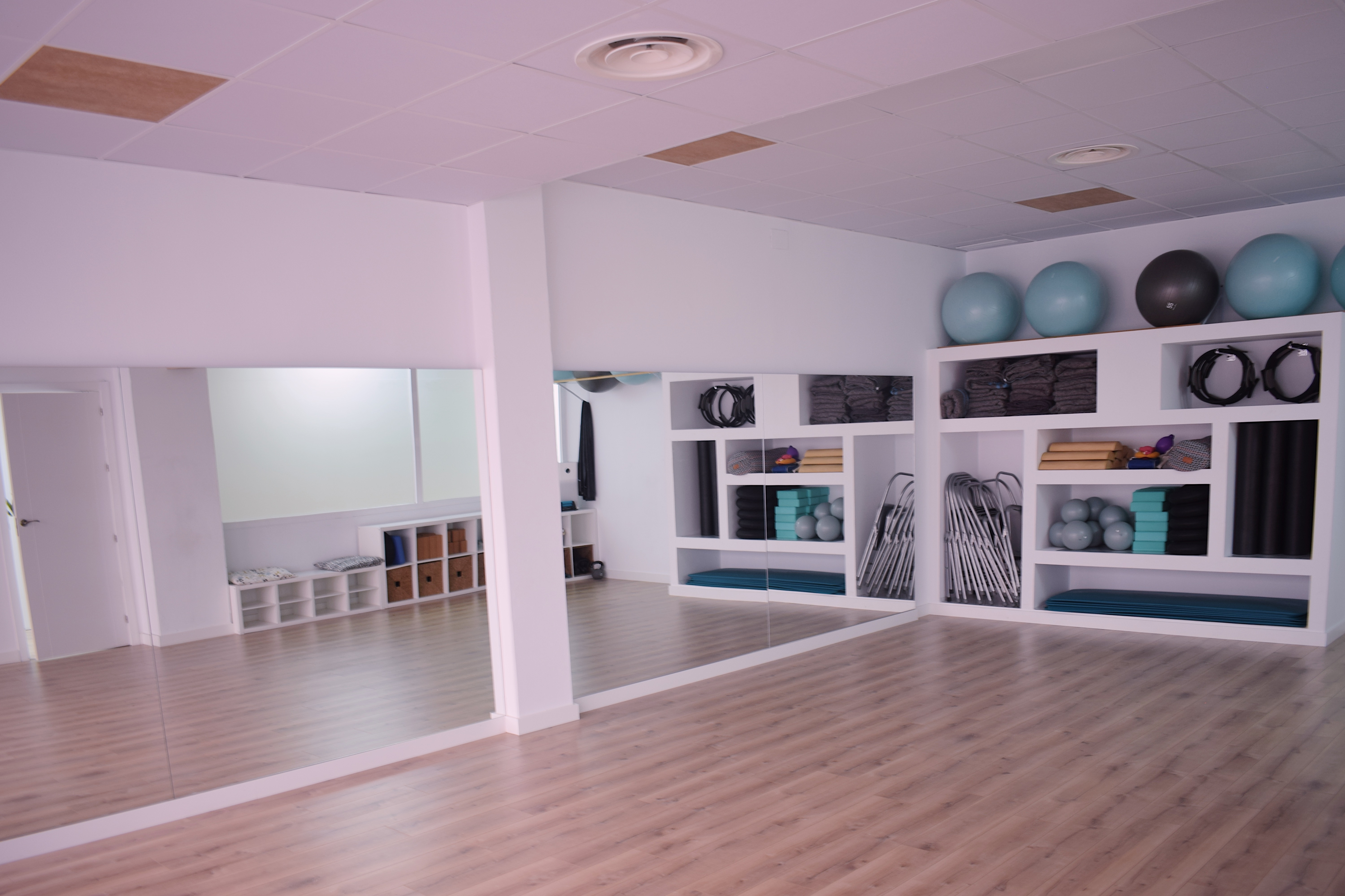 Sala de actividades grupales con espejos y estanterías con colchonetas, bloques y pelotas de pilates